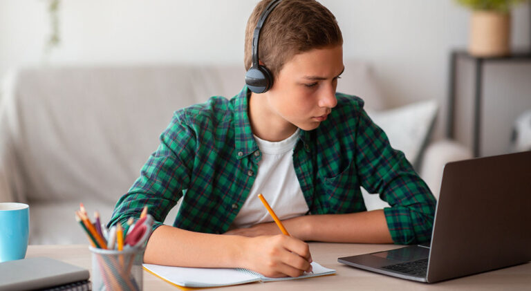 Pensive school boy with earphones studying online from home