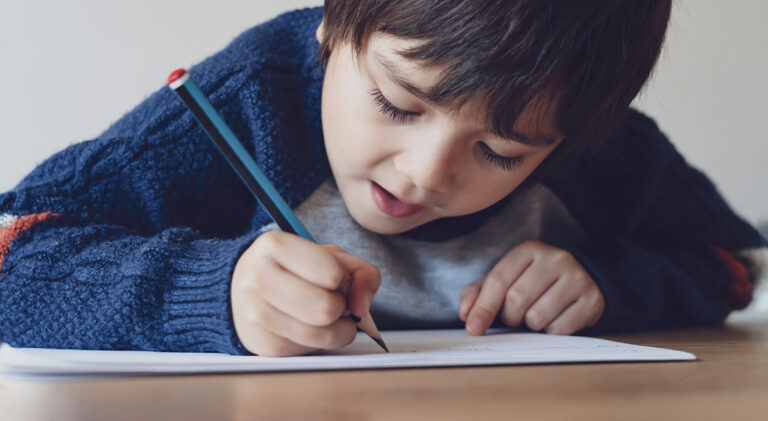 Portrait of school kid boy siting on table doing homework, Happy