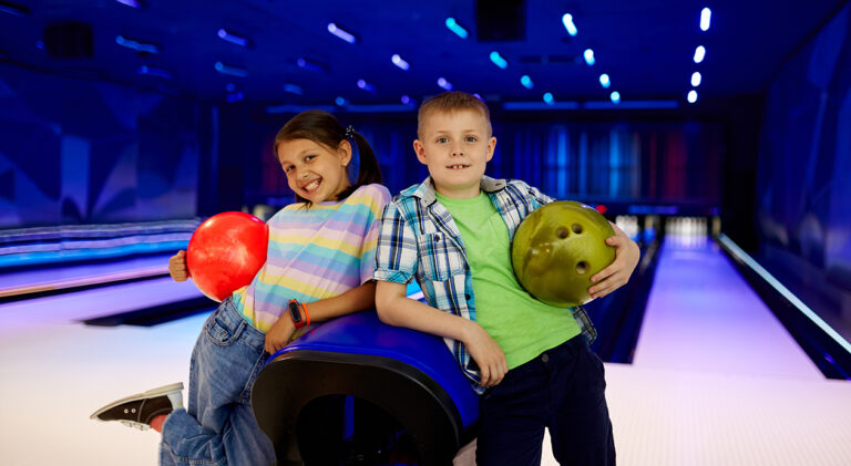 Two children with balls poses in bowling alley