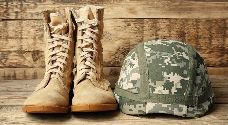 Pair of combat boots and military helmet on wooden background, c