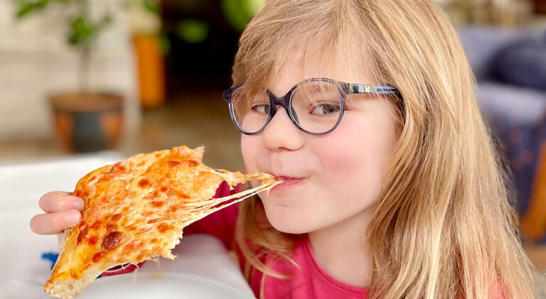 Little Preschool Girl eating a piece of Pizza. Happy Child biting pizza with cheese