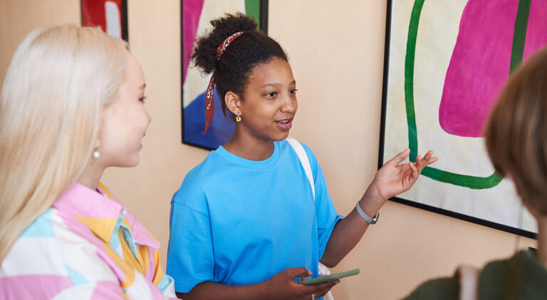 Black teenage girl discussing art with group of friends in art gallery